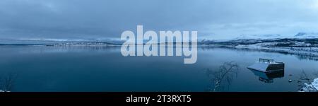 Panoramic view of Torneträsk lake with snowy mountain under a dark cloudy sky in winter in the Abisko National Park Stock Photo