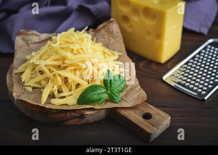 Grated cheese  on a cutting  board with fresh basil  on a wooden background Stock Photo
