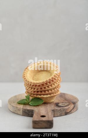 Empty tartlet shells on wooden cutting board on light background Stock Photo