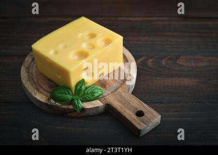 Cheese with holes large and small at cutting board on wooden background Stock Photo