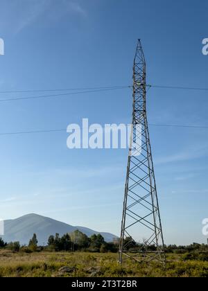 Overhead line pylon, high voltage pylon in meadow with mountains on background at summer sunny day, near Oricum, Albania Stock Photo