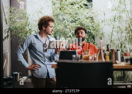 Young architects and engineers discuss project details over blueprints at a coffee bar, ensuring successful construction and urban planning. Stock Photo