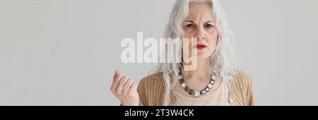 Worried senior woman with long loose hair stands in studio Stock Photo