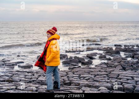 Woman in bright yellow jacket walking alone on the seaside on cold winter day. Travel  Lifestyle concept Stock Photo