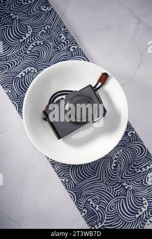A retro style camera is placed on a white ceramic dinner plate Stock Photo