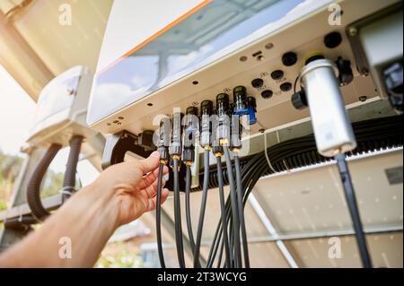 Professional worker connecting wires to solar inverter. Pov of configuring inverter. Male worker turning on PV battery. Stock Photo