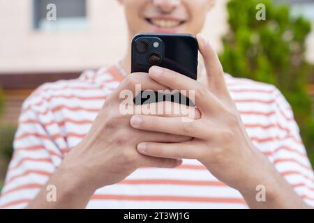 close-up of smiling young man using smartphone app outdoors. Stock Photo