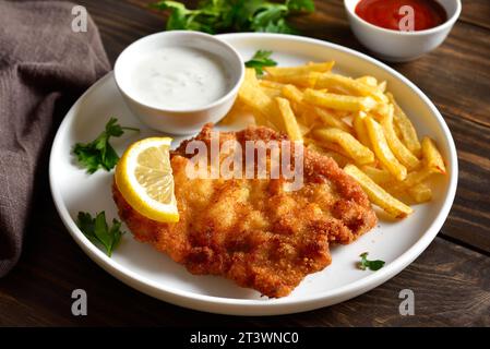 Breaded wiener schnitzel with potato fries and sauce on wooden table. Close up vuew Stock Photo