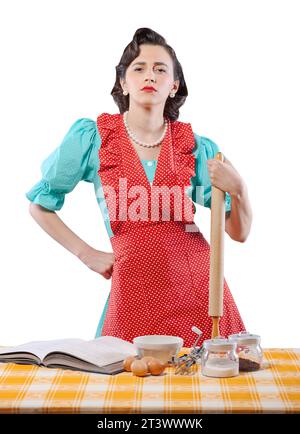 Confident vintage style housewife in the kitchen, she is posing with a rolling pin Stock Photo