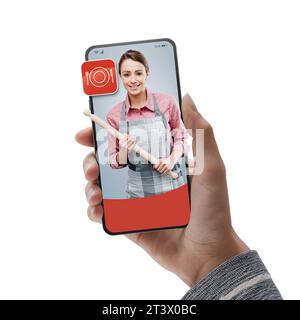 Female cook holding a rolling pin on smartphone: hire professionals online Stock Photo