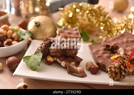 Detail of chocolate with hazelnuts on white ceramic plate on wooden table with Christmas decoration. Elevated view. Stock Photo