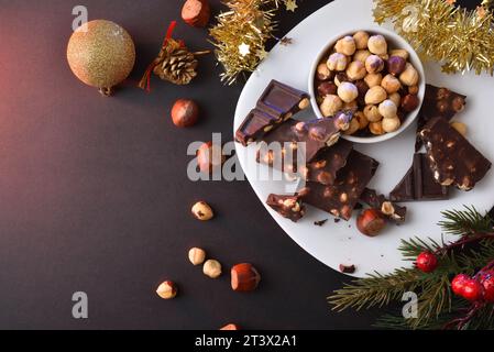 Chocolate with hazelnuts and dried fruit in a white plate on a black table with red lighting decorated christmas decorative element. Top view. Stock Photo