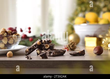 Portions of chocolate with hazelnuts and nuts in a glass bowl on a wooden table decorated in a living room with a window and a Christmas tree in a liv Stock Photo