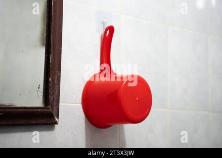 Indonesian gayung or water sadle hanged on the wall next to the old mirror. It is used in Indonesia to take a shower or take a bath. Gayung mandi Stock Photo