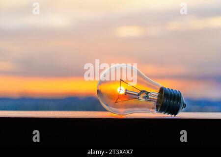 Glowing light bulb set against the backdrop of a setting sun. Clean energy and sustainability related concept. Stock Photo