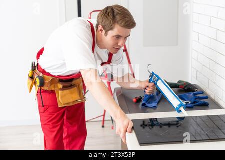 Gloved craftsman installs hob in kitchen. Household Appliance Installation Services Concept Stock Photo