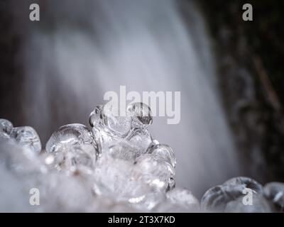 Closeup photo of round ice shapes icicles with blurred waterfall in the background, textured ice formations, frozen icy mountain stream Stock Photo