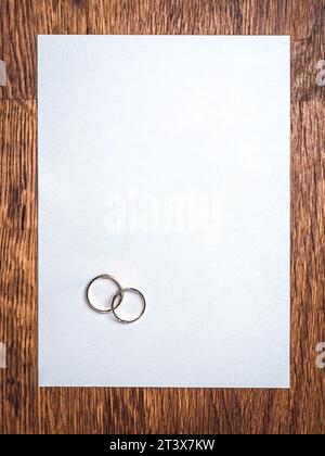 Simple flat lay mockup of a pair of wedding rings on a blank textured paper and wooden table background Stock Photo