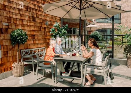 Senior man and women talking while sitting at dining table on sunny day Stock Photo