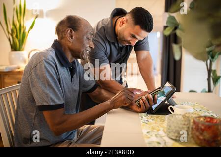 Male nurse assisting senior man in using digital tablet and smart phone at nursing home Stock Photo