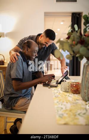 Happy male nurse assisting senior man in using digital tablet and smart phone at nursing home Stock Photo