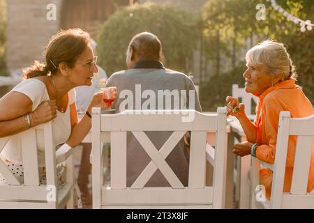 Retired senior women talking behind man while sitting at back yard Stock Photo