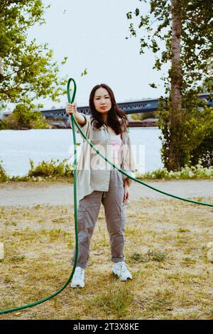 Full length portrait of confident young woman holding garden hose Stock Photo