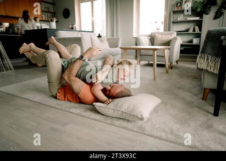 Full length of father lying on carpet while embracing son in living room at home Stock Photo