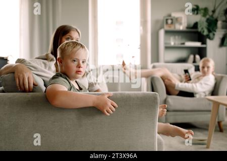 Boy with down syndrome watching TV by mother sitting on sofa at home Stock Photo