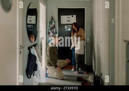 Boy embracing mother by father kneeling in mudroom at home Stock Photo