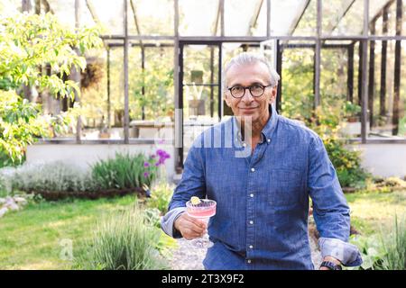 Portrait of smiling retired senior man with drink at back yard Stock Photo