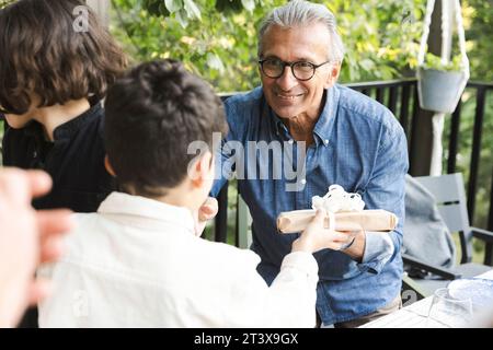 Smiling senior man giving gift to grandson during dinner party Stock Photo