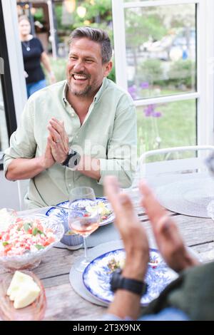 Cheerful mature man clapping while sitting at dining table Stock Photo