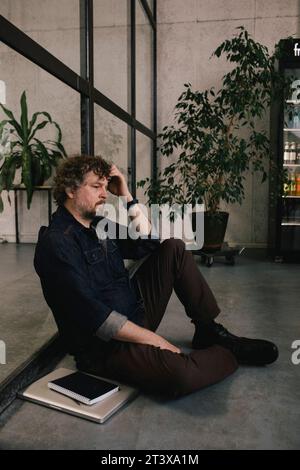 Side view of depressed professional businessman leaning on glass wall at office Stock Photo