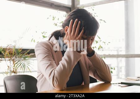 Exhausted businesswoman sitting with head in hands at office Stock Photo