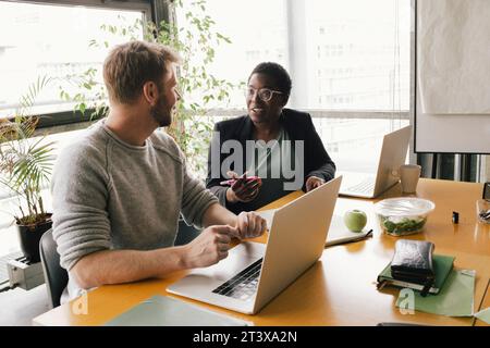 Smiling businesswoman discussing with businessman while sitting at desk in office Stock Photo