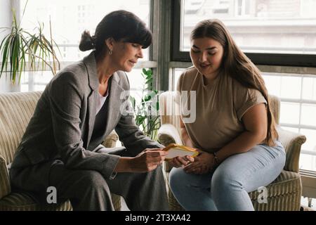 Businesswoman discussing over placard with non-binary professional while sitting at office Stock Photo