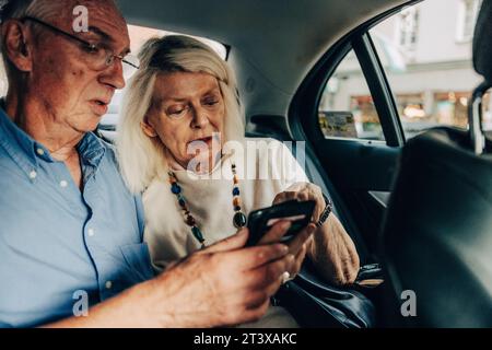 Senior couple using smart phone while sitting in taxi Stock Photo