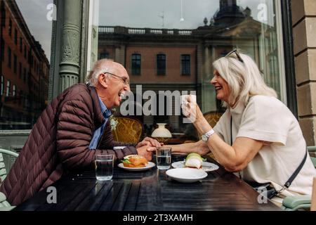 Happy senior man holding hand of woman while sitting together at sidewalk cafe Stock Photo