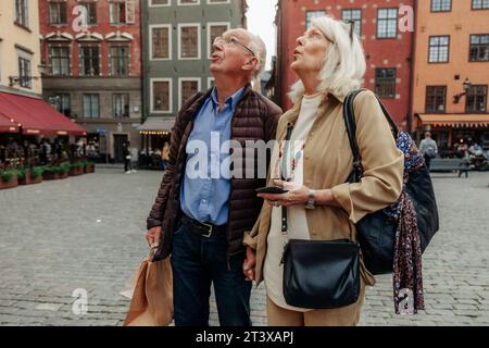Amazed senior couple looking up while standing together in city Stock Photo