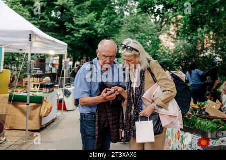 Senior man and woman using smart phone while standing at market place Stock Photo