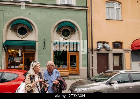 Confused senior man and woman looking away while crossing against building Stock Photo