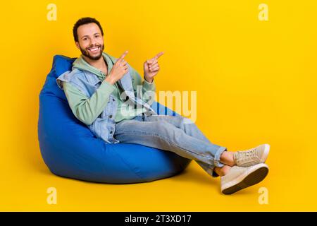 Full body length size cadre of wearing khaki sweatshirt denim waistcoat sit pouf direct fingers novelty isolated on yellow color background Stock Photo