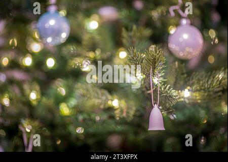A small, decorative bell, among silver baubles, hanging on a Christmas tree, with fairy lights, illuminating the scene Stock Photo