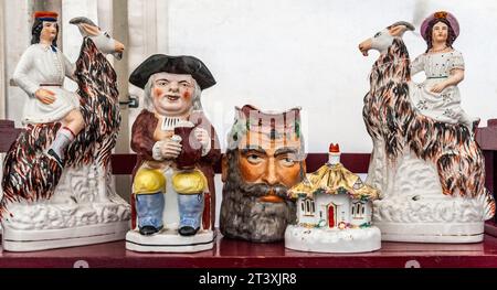 Antique Staffordshire china ornaments for sale at a country antiques fair, including a Toby Jug and a pair of female figures riding on goats (UK) Stock Photo