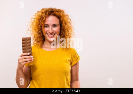 Portrait of happy cute ginger woman holding chocolate bar. Stock Photo