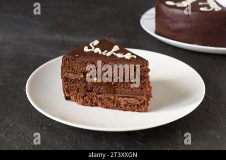 Chocolate cake Sacher with apricot jam on white plate. Traditional Austrian dessert. Dark background. Stock Photo