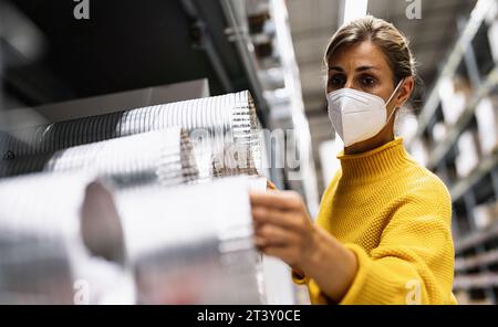 woman with face mask examines silver ventilation tubes in a warehouse or store setting.  Corona safety Concept image Stock Photo