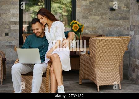 Couple, hugging, are sitting in a wicker chair on terrace Stock Photo