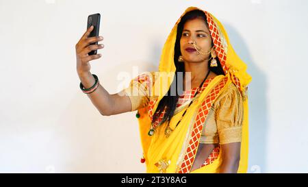 Indian ethnicity woman taking selfie on karwa chauth hindu festive of lights, wearing traditional yellow saree isolated on white background. during ka Stock Photo